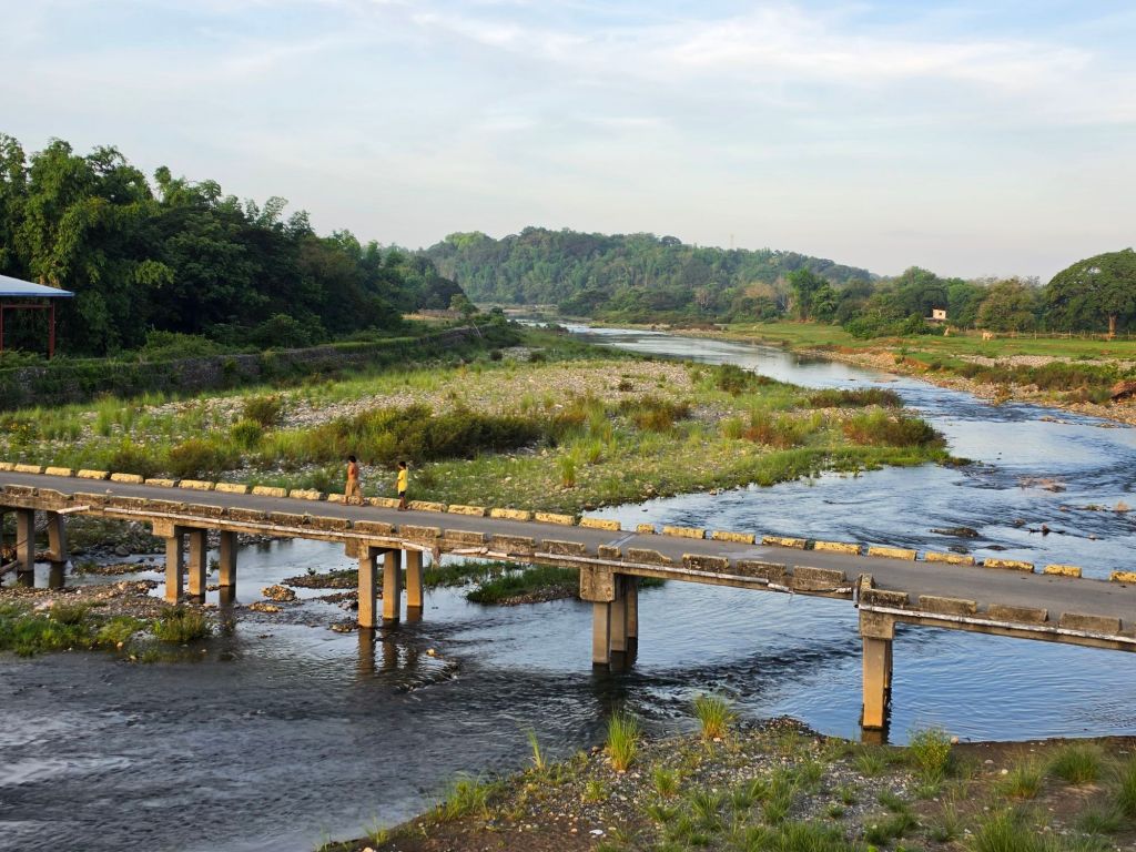 A scenic view of a river with a bridge crossing over it, surrounded by lush greenery and a rocky riverbed.