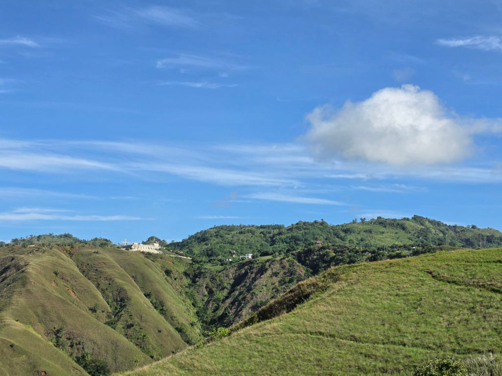 Scenic view of rolling green hills under a clear blue sky with a single cloud.